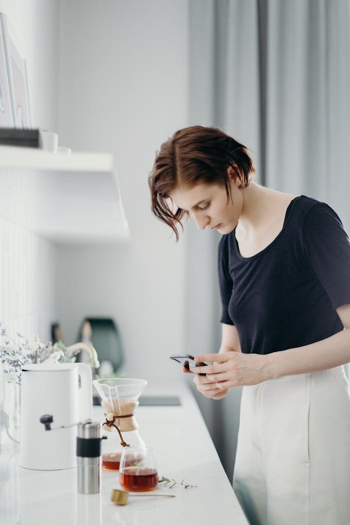 A woman captures a photo of a coffee setup in a modern kitchen.